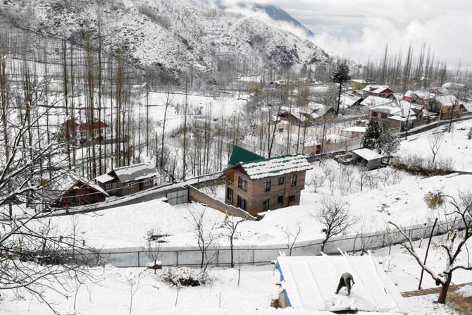 A villager clears snow from the roof of a house following fresh snowfall on the outskirts of Srinagar yesterday. Pic/AFP
