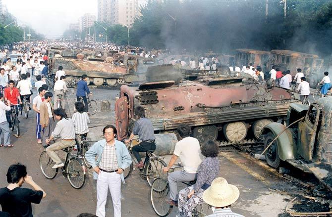 People gather around armoured vehicles burnt by protesters during clashes with soldiers near Tiananmen Square in June 1989. Pic/AFP