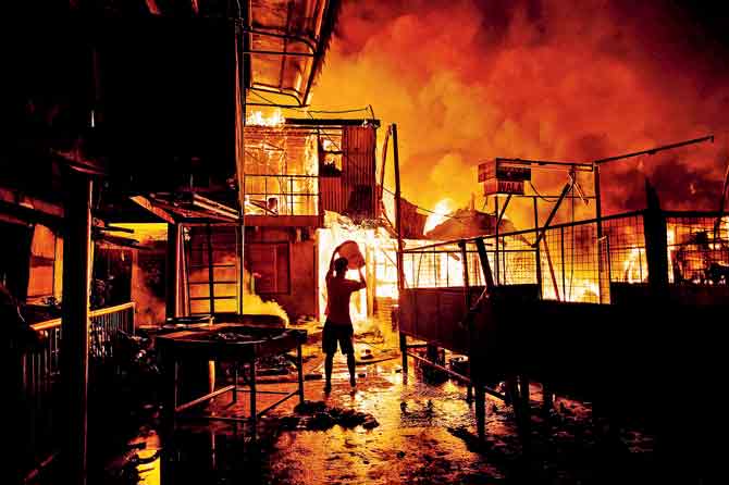 A resident pours water on a fire as it destroys hundreds of houses at an informal settlers community in Delpan, Tondo, Manila. Pic/AFP