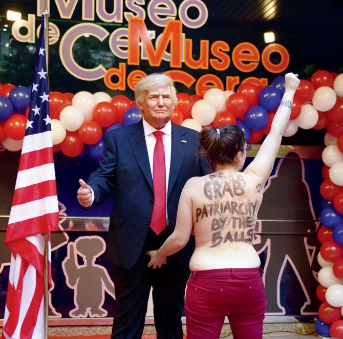 A topless Femen activist with a sign painted on her back raises her fist as she protests in front of the wax statue of US President-elect Donald Trump at the Wax Museum of Madrid on Tuesday. Pic/AFP