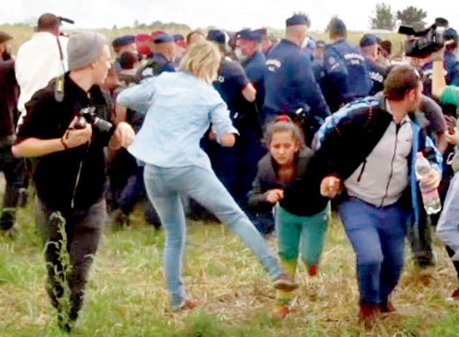 Petra Laszlo (inset) kicks a child as she runs with other migrants from a police line during disturbances in southern Hungary. Pic/AFP