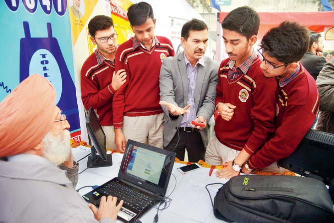 Indian students listen to a Unique Identification Authority of India officer, Anil Bhatia (C) as he withdraws money from his bank account with an Aadhaar card during a Digi Dhan Mela, held to promote digital payment in Amritsar. Pic/ AFP