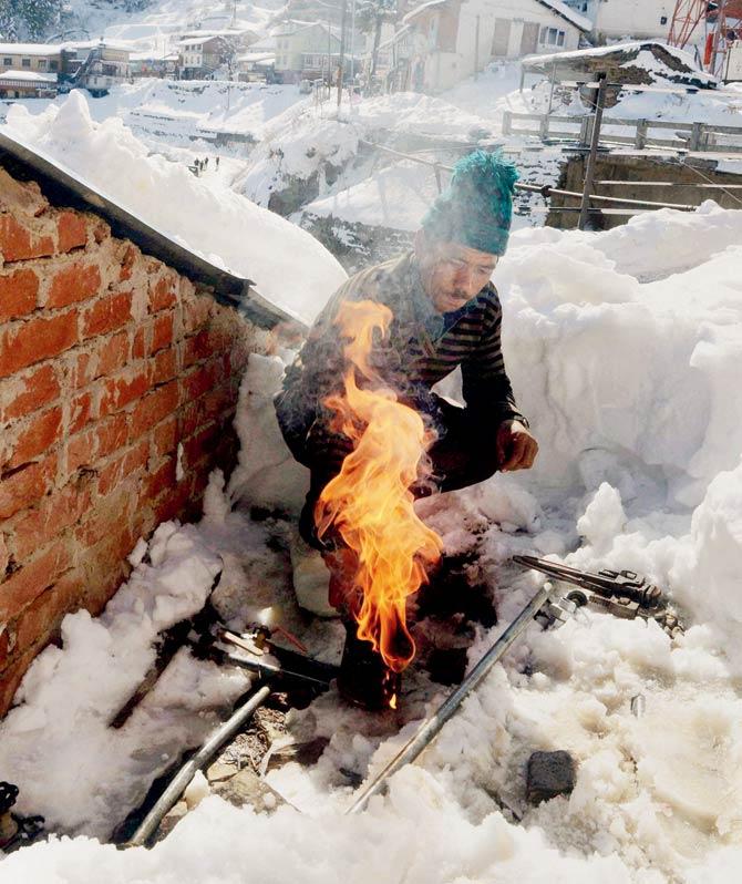 A man uses fire to clean a frozen water pipeline in Shimla. Pic/PTI