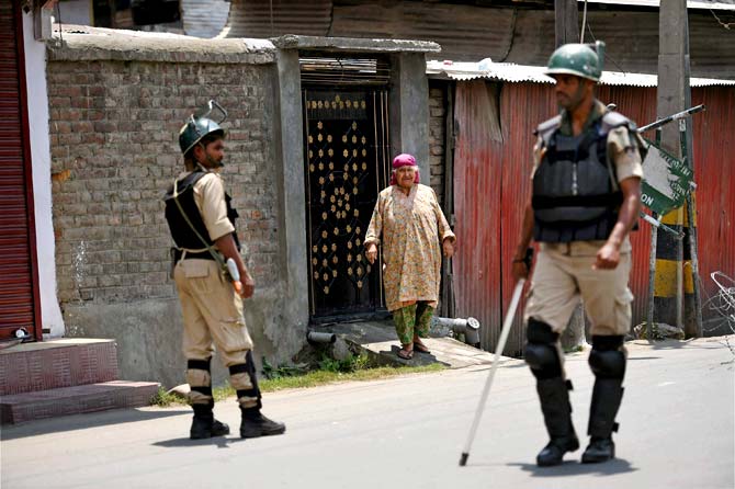An elderly woman looks on as security jawans stand guard during restrictions in down town Srinagar. Pic/AFP