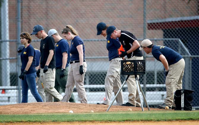 Investigators from the FBI comb the infield while looking for evidence at Eugene Simpson Field, the site where a gunman opened fire in Alexandria. Pic/AFP