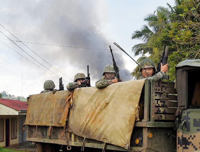 Philippine Marines aboard a truck drive past, as smoke billows after rockets were fired at militant positions in Marawi. Pic/AFP