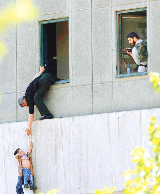 A man hands a child to a security guard from Iran