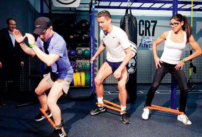 Ronaldo gives his legs a workout alongside two trainers at the unveiling of CR7 gym