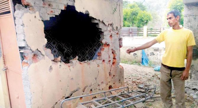 A resident living near the border points out damage caused to the wall of a government school by mortal shelling from Pakistan, at Jhanghar yesterday. Pic/PTI