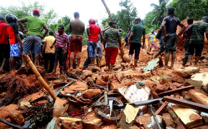 Sri Lankan military rescuers and villagers stand on the debris of a house that was destroyed in a landslide. Pic/AP, PTI