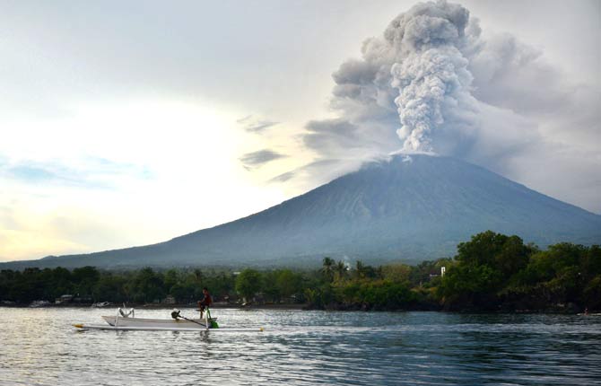 A fisherman drives a traditional boat as Mount Agung erupts seen from Kubu sub-district in Karangasem Regency on Indonesia