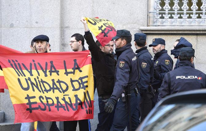 Spanish police stand guard next to two men holding Spanish flags reading "Long live Spanish unity" as the former speaker of Catalonia