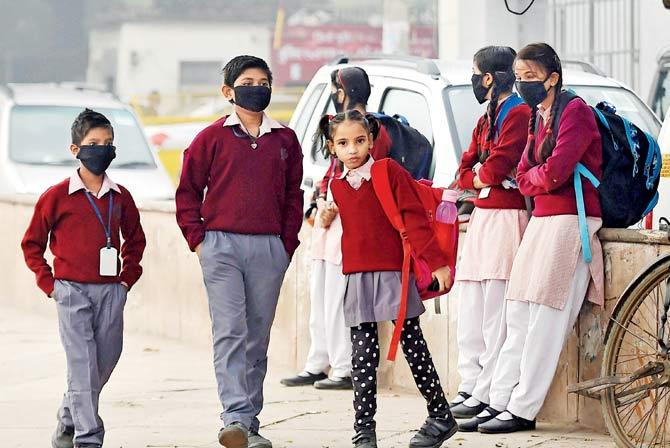 Children wear masks as protection against smog and air pollution, while waiting for their school bus in New Delhi. Pic/PTI