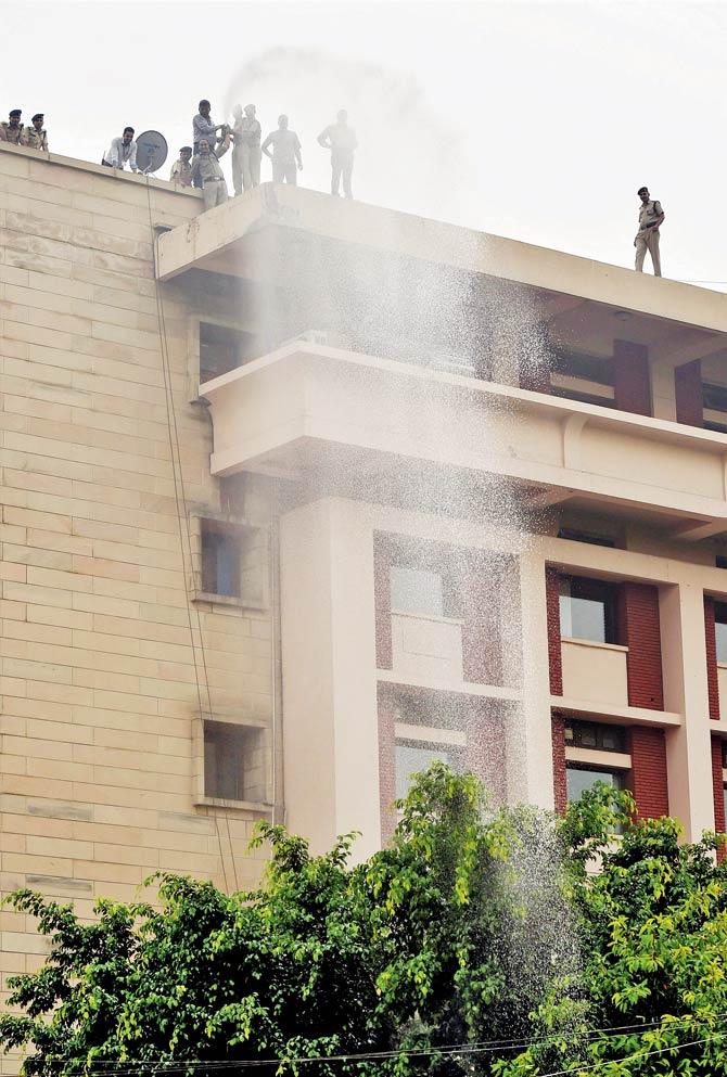 RPF jawans use fire fighting equipment to sprinkle water on trees to remove dust at Rail Bhawan in New Delhi, on Saturday. Pic/PTI