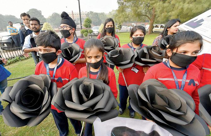 Children wearing air pollution masks, hold replicas of black roses as they attend a demonstration to spread awareness about the problem of air pollution, on Children