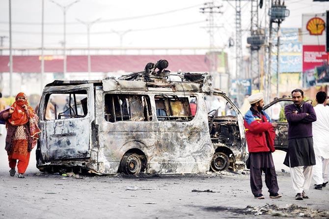 A Pakistani woman walks past a burnt vehicle near the site of a protest in Rawalpindi. pic/afp