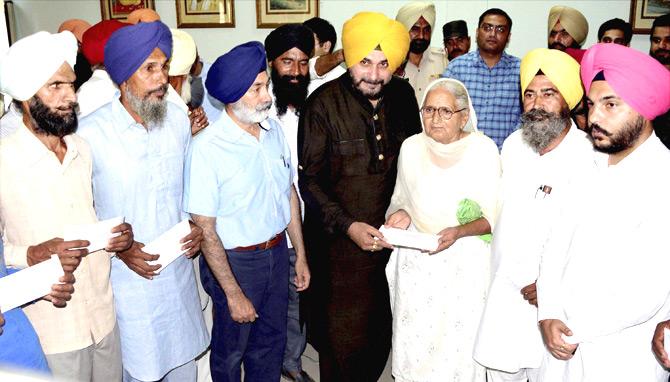 Punjab Tourism and Cultural Affairs Minister Navjot Singh Sidhu hands over cheques to farmers who have lost their crops to fire, in Amritsar on Wednesday. Pic/PTI