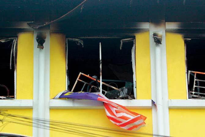 A Malaysian national flag flutters outside burnt windows of the school in Kuala Lumpur
