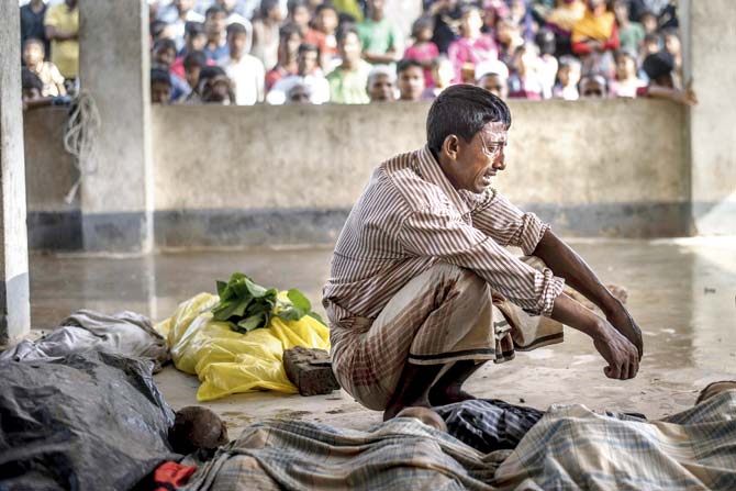 A Rohingya Muslim refugee mourns beside the bodies of his three children at a school in Cox