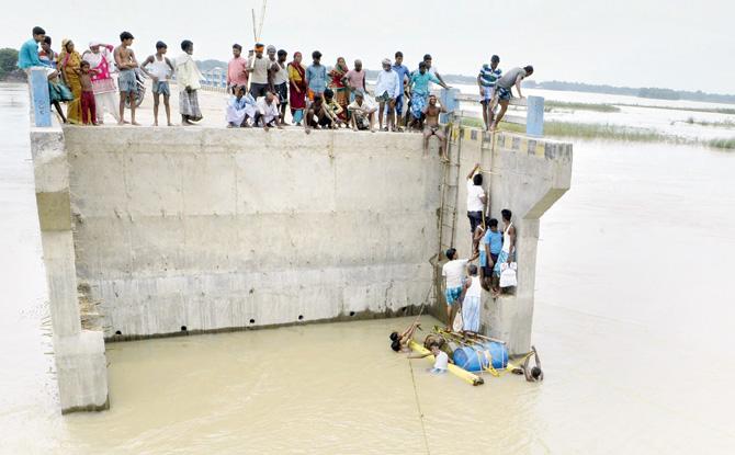 Villagers cross flood waters with the help of rope and empty canisters next to a washed away portion of a bridge at Purnia. Pic/AFP