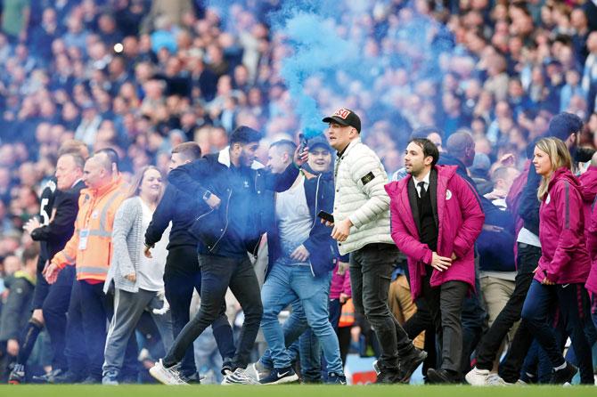 Man City fans celebrate on the pitch at the Etihad Stadium after their team