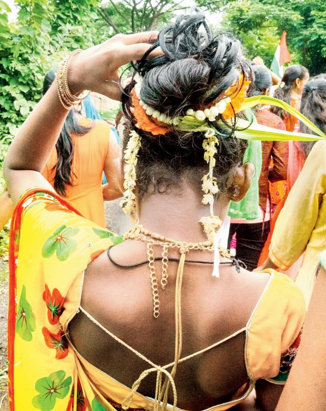 A Warli woman ties her hair into a bun with flowers tucked in