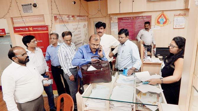 ED officers inspect documents after seizing cash, jewellery and bonds worth crores during a raid in Thane late on Monday. Pic/PTI