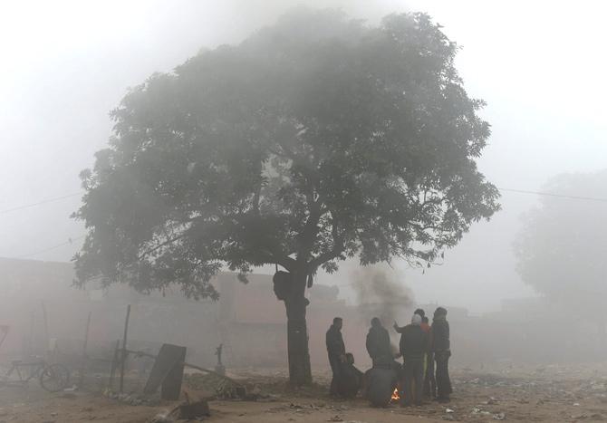 People sit around a fire to keep themselves warm during a foggy morning, in Delhi on Monday. Pic/PTI