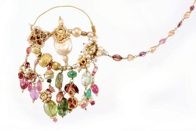 Nath from West Rajasthan, Barmer district, early 20th century: An elaborate gold bali or balu nose ring with its original chain which can be hooked to the hair or head cloth to give support the weight. The bali is decorated with different colours of irregular tourmaline beads, pearls and gold beads, and this style reflects the jewellery design of early Bukhara region in Uzbekistan. In Hinduism, the nose ring is a symbol of being married. Getting the nose pierced is also seen as paying respect to Goddess Parvati. 