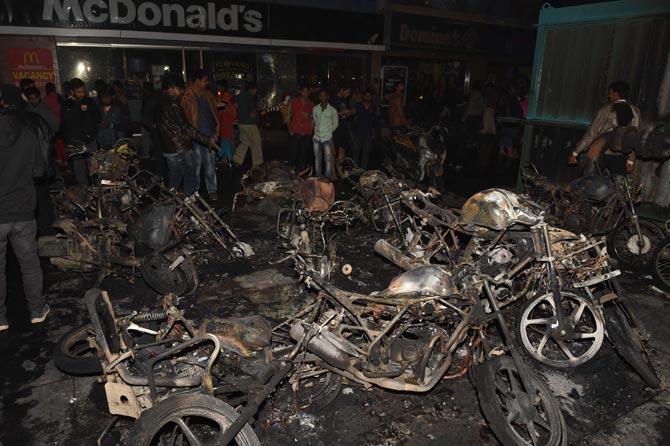 People walk around the charred remains of parked motorcycles, burned during protests against the film Padmaavat, late on January 23, 2017 at the Himalaya Mall in Ahmedabad. Pic/PTI