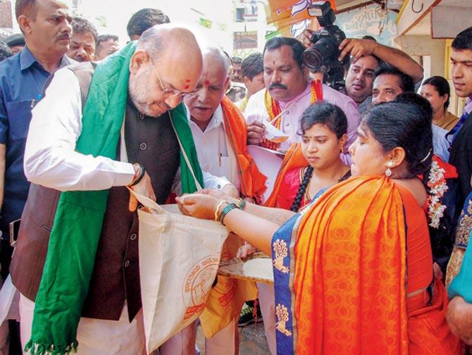 Amit Shah collects foodgrains from a farmer family during a campaign at Doddabathi village on Tuesday. Pic/PTI