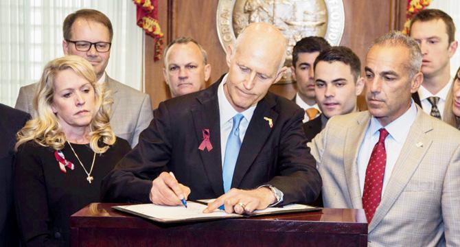 Rick Scott (centre) is joined by colleagues and parents of school shooting victims as he signs the bill