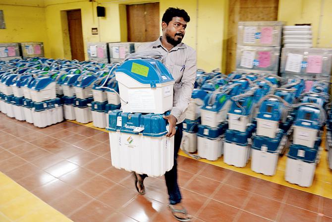 A polling official carries VVPAT machines to load data of symbols at a distribution point ahead of the second phase of the election, in Chennai