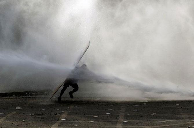A demonstrator is hit by a riot police water cannon spray during a protest against the government in Santiago on November 18, 2019. President Sebastian Pinera condemned on Sunday for the first time what he called abuses committed by police in dealing with four weeks of violent unrest that have rocked Chile and which has left 22 people dead and more than 2,000 injured. Chileans have been protesting social and economic inequality, and against an entrenched political elite that comes from a small number of the wealthiest families in the country, among other issues.