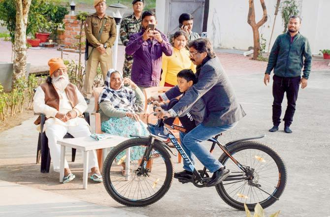 Jharkhand Mukti Morcha working president Hemant Soren rides a bicycle at his residence in Ranchi on Monday as his father and party chief Shibu Soren and mother Ripu Soren look on. Pic/PTI