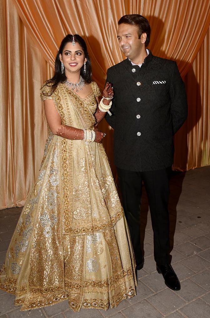 Isha Ambani and Anand Piramal hosted a grand wedding reception at BKC in Mumbai on December 14, 2018. For the wedding reception, Anand Piramal sported a black bandhgala, while the bride Isha Ambani was wearing a golden lehenga paired with a unique white colour choora and traditional jewellery and looked absolutely stunning in it.
In picture: The new couple shares a laugh as Anand seems to be in awe of his wife Isha.