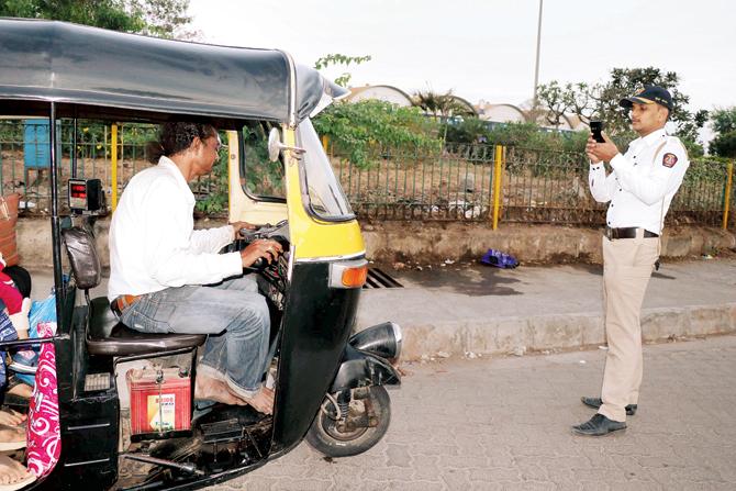 A cop takes down the registration number of the auto before issuing an e-challan to the driver for not wearing a uniform