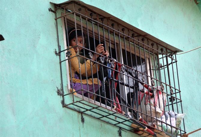 In photo: A young girl watches her area through the window amid total lockdown.