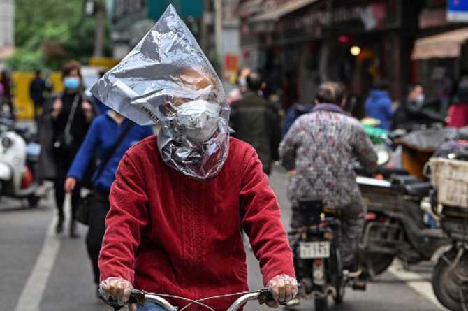 A man wearing a face mask and a plastic bag on his head rides a bicycle on a street in Wuhan, China's central Hubei province.