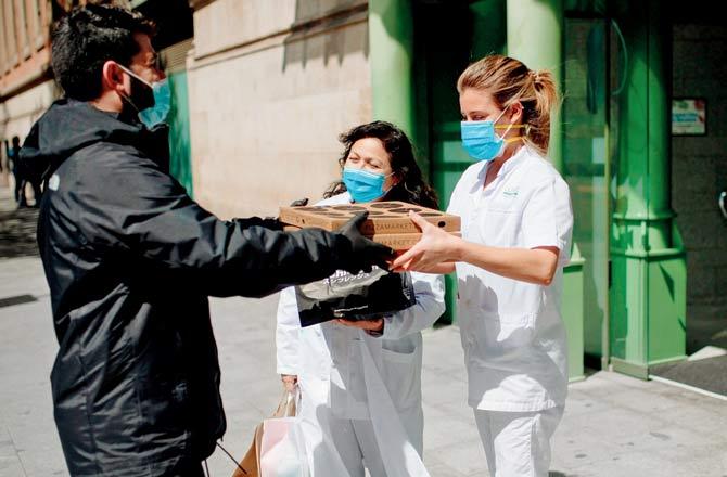 A delivery person working for Delivery4Heroes hands pizzas to healthcare workers at a hospital in Barcelona. Pic/AFP