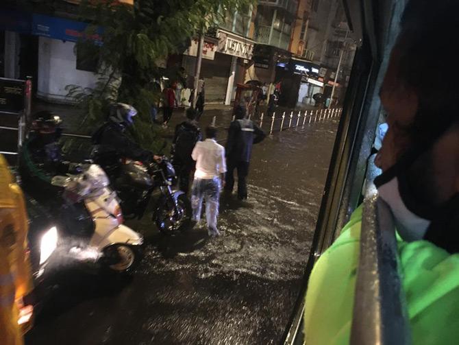 In picture: Motorists and pedestrians wade through waterlogged streets while a man looks on from the window of a bus.