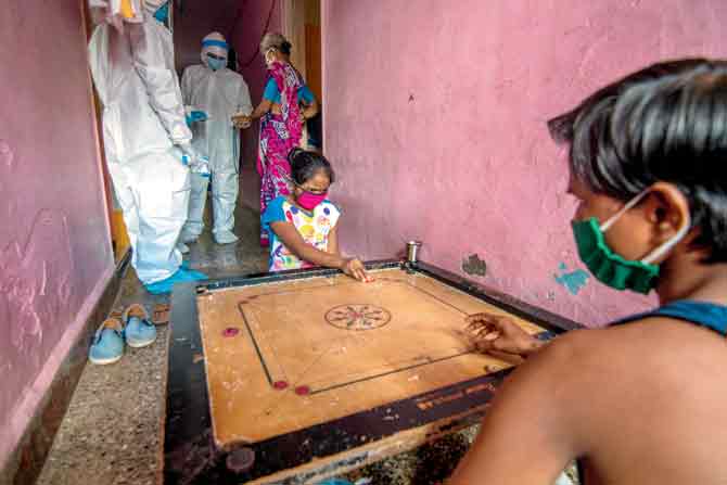 Residents of Chikuwadi, Mankhurd, play carrom using precautions while healthcare workers carry out temperature tests, last week. PIC/GETTY IMAGES