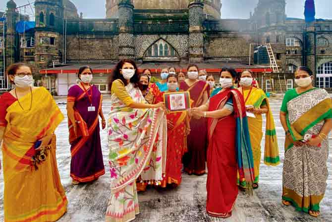 Staff dressed in handloom sarees pose with a stamp