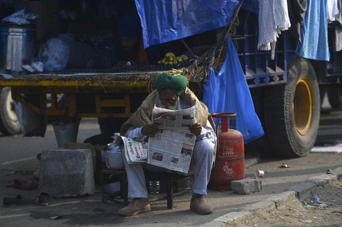 In this picture taken on December 5, 2020 a farmer reads a newspaper next to a vehicle along a blocked a road by police to stop farmers from marching to New Delhi to protest against the central government's recent agricultural laws, at the Delhi-Haryana state border in Kundli. Photo: AFP