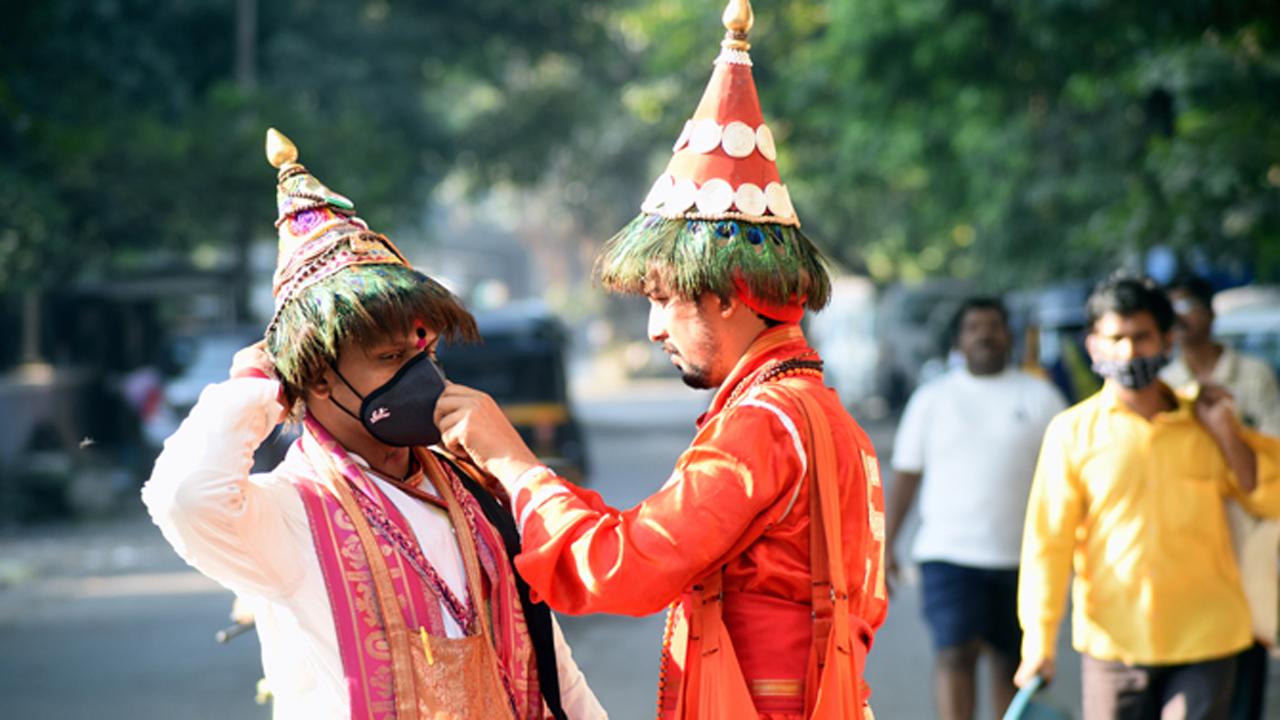 A member of the Vasudev community, wandering minstrels who sing Bhakti songs, helps his co-singer wear the mask, at Thane East.
Photo: Sameer Markande