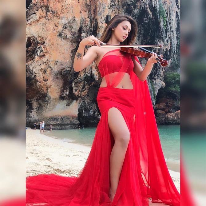 In photo: Mimi Chakraborty looks chic in this stunning off-shoulder boho dress in hues of red as she plays the violin amidst a picturesque location