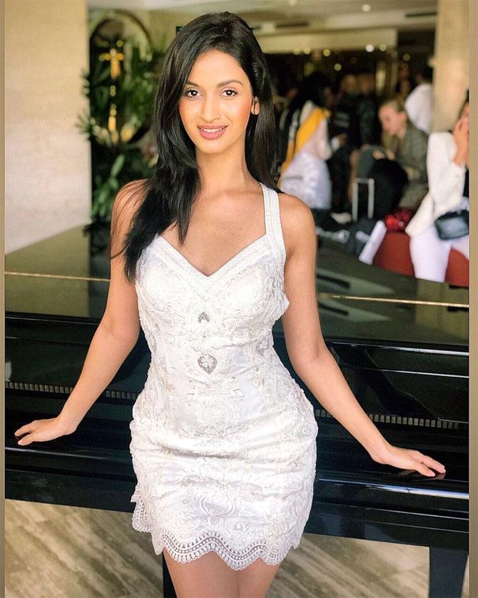 The model looks stunning in a white netted dress. She wears minimal makeup and accessories but manages to strike an impression with her brightly lit smile.