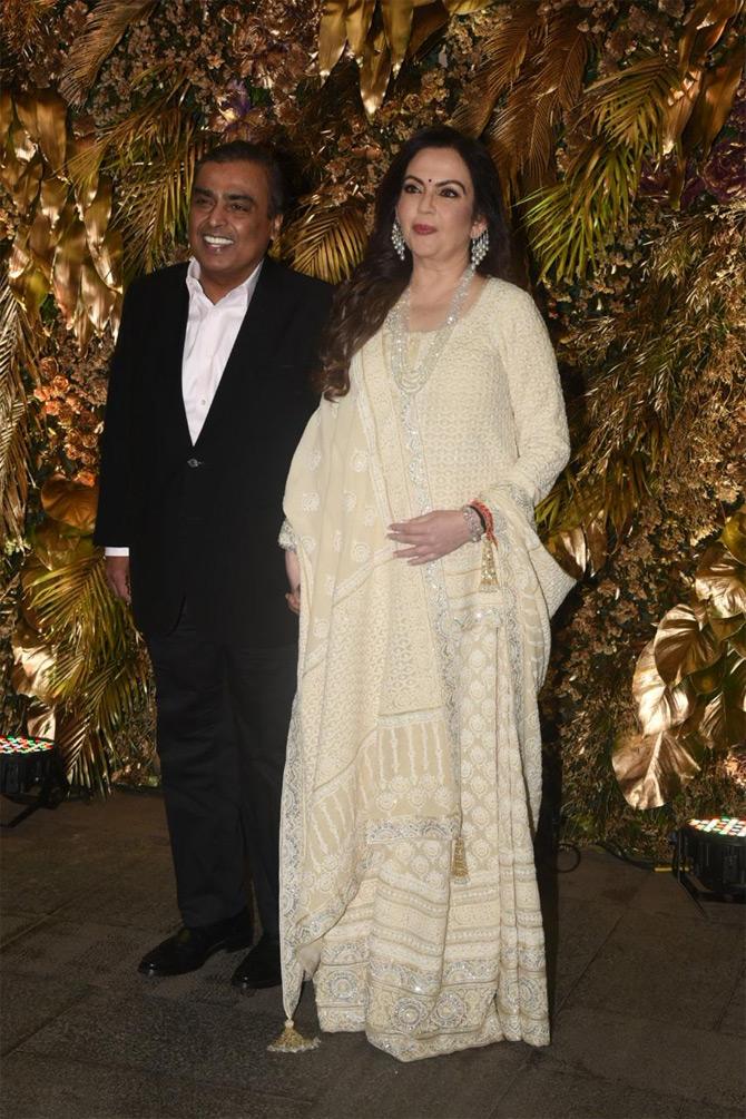 For the wedding bash, Mukesh Ambani opted for a black suit with a white shirt as he posed for the paparazzi at the bash held at The St Regis hotel. While his wife Nita Ambani donned an elaborate blouse and teamed it with a white and cream full-sleeve lehenga. She completed her look with a long neckpiece, diamond earrings, and minimal accessories. With subtle makeup and her long wavy hair parted on one side, Nita looked ethereal in an ethnic wear.