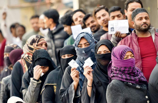 Voters stand in queues to cast their vote during the Delhi Assembly elections