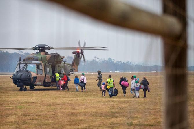  The bushfires have caused many residents to evacuate due to the threat of wildfires in their locality. In picture: Evacuees board a Royal Australian Navy MRH-90 helicopter at Mallacoota, as bushfires threaten the area